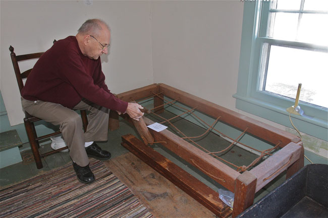 Mattituck Historical Society curator Norman Wamback demonstrates how a parent would tighten the ropes on a child's bed. The mattress was supported by the rope lattice.