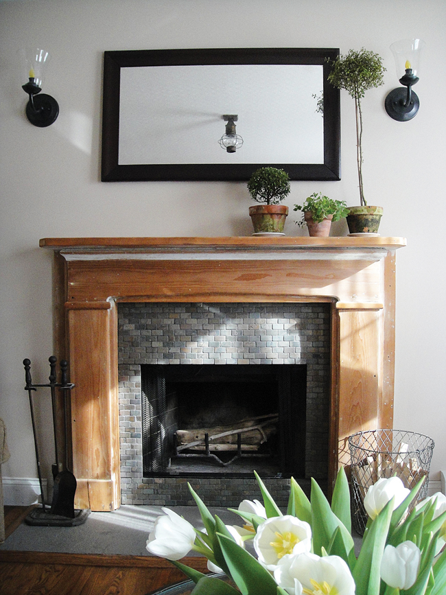 A mantel that incorporates both simplicity and asymmetry with potted topiaries and a large rectangular mirror. (Credit: Lori Guyer)